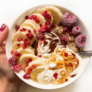 Bowl of oatmeal with banana slices, berries, yogurt, and chocolate sauce.