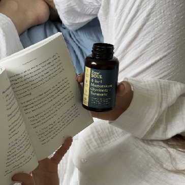Person in white holding a book and a supplement bottle.