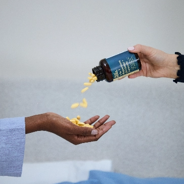 Person pouring yellow pills from a bottle into another person's hand.