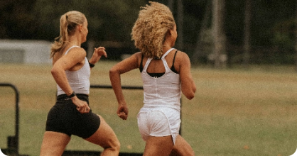 Two women running outdoors on a grassy field.
