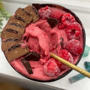 Bowl of pink smoothie with raspberries, chocolate pieces, and a spoon.