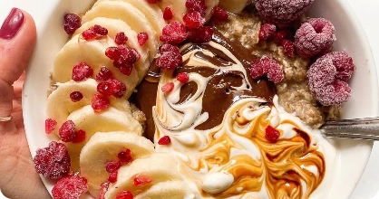 Bowl of oatmeal with banana slices, raspberries, and swirled chocolate and yogurt.