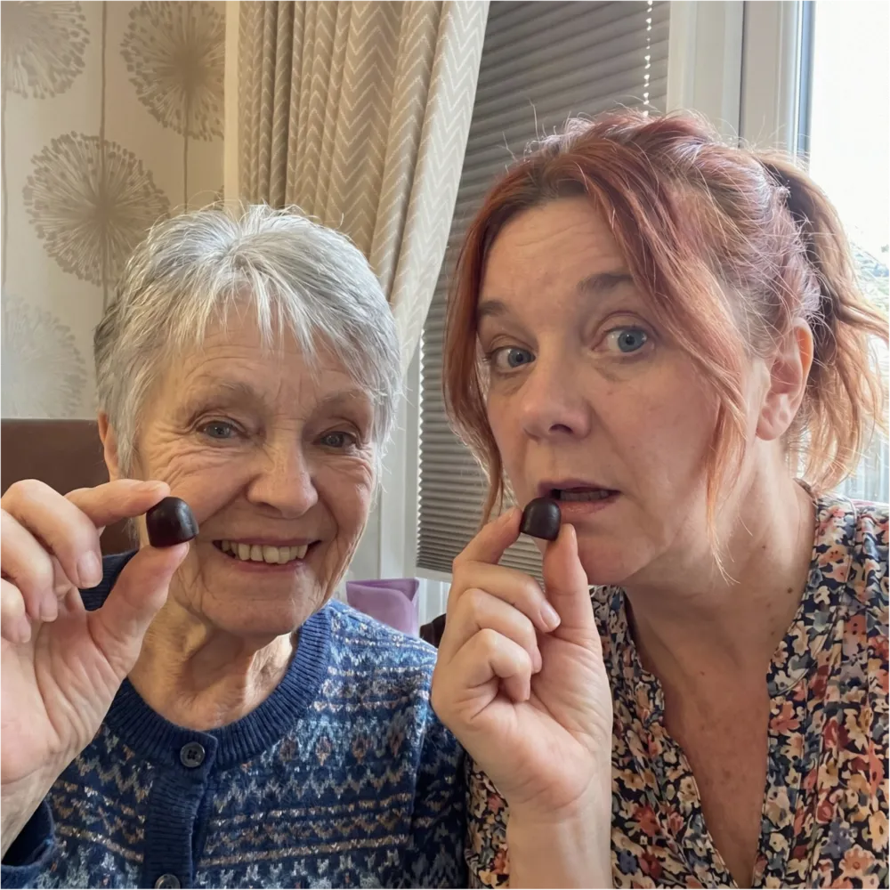 An older woman and a younger woman pose for the camera, each holding a piece of chocolate.