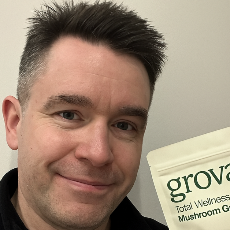 Man with short hair holding a pouch of Grova Total Wellness Mushroom Gummies and smiling confidently.