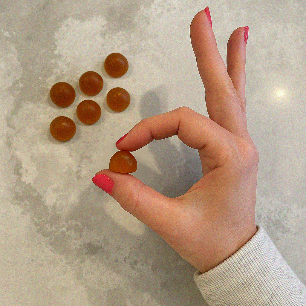 Hand holding a grova mushroom gummy with more mushroom gummies on a marble surface