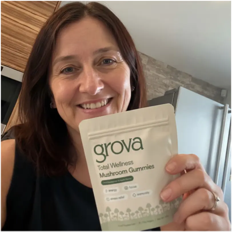 Person smiling, holding a package labeled 'grova Total Wellness Mushroom Gummies'.