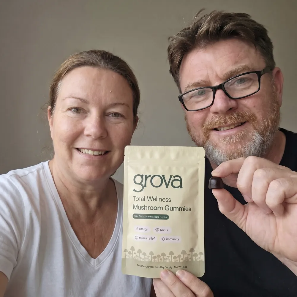 A man and woman smiling while holding a pouch of Grova mushroom gummies and a single gummy.