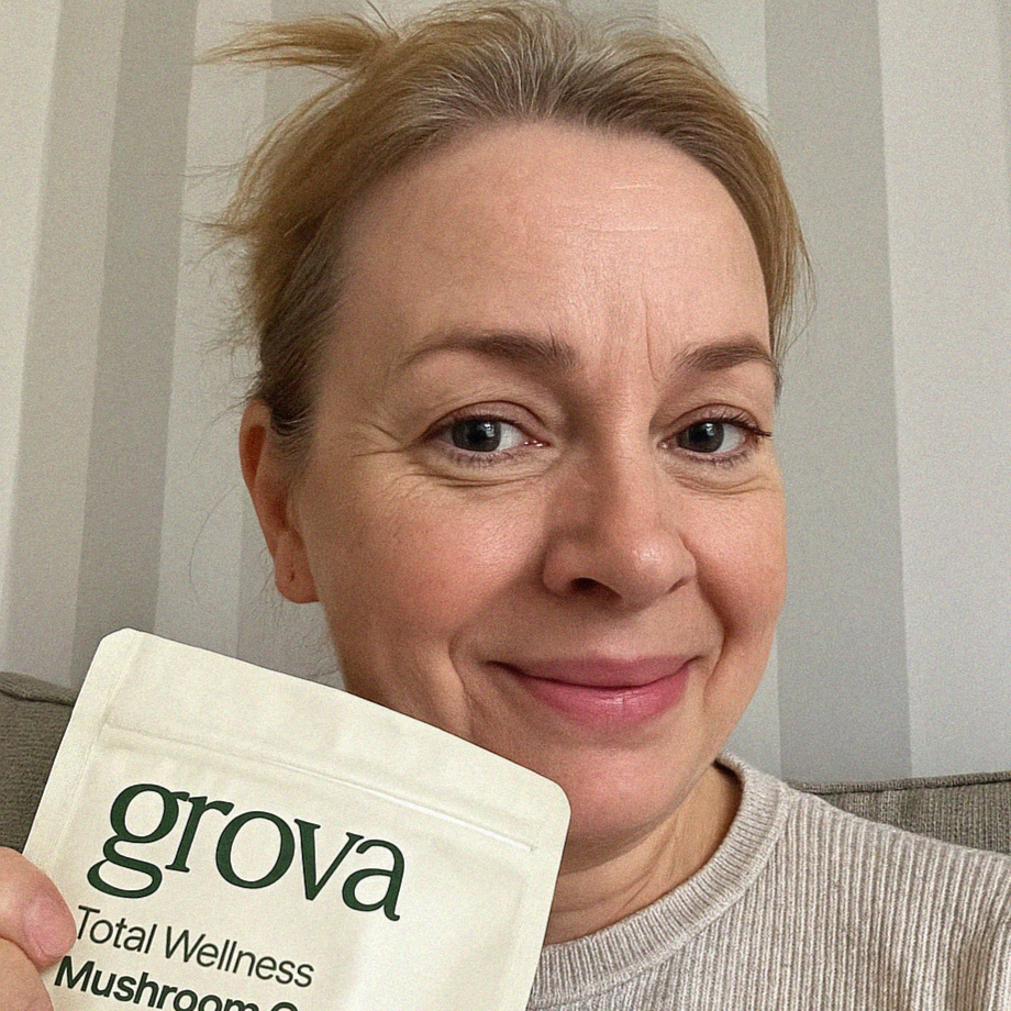 Smiling woman holding a Grova Total Wellness Mushroom Gummies pouch, sharing her experience.