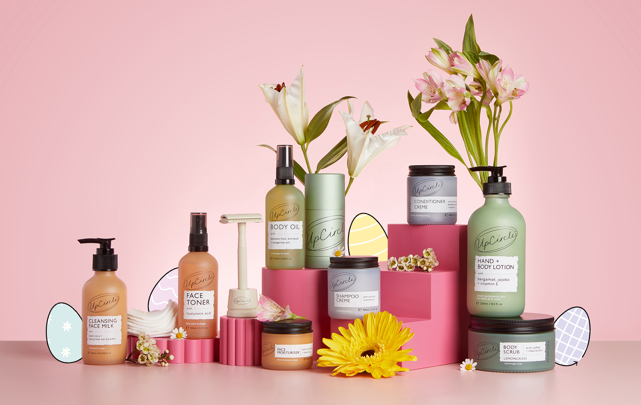 Assorted skincare products with flowers on a pink background.