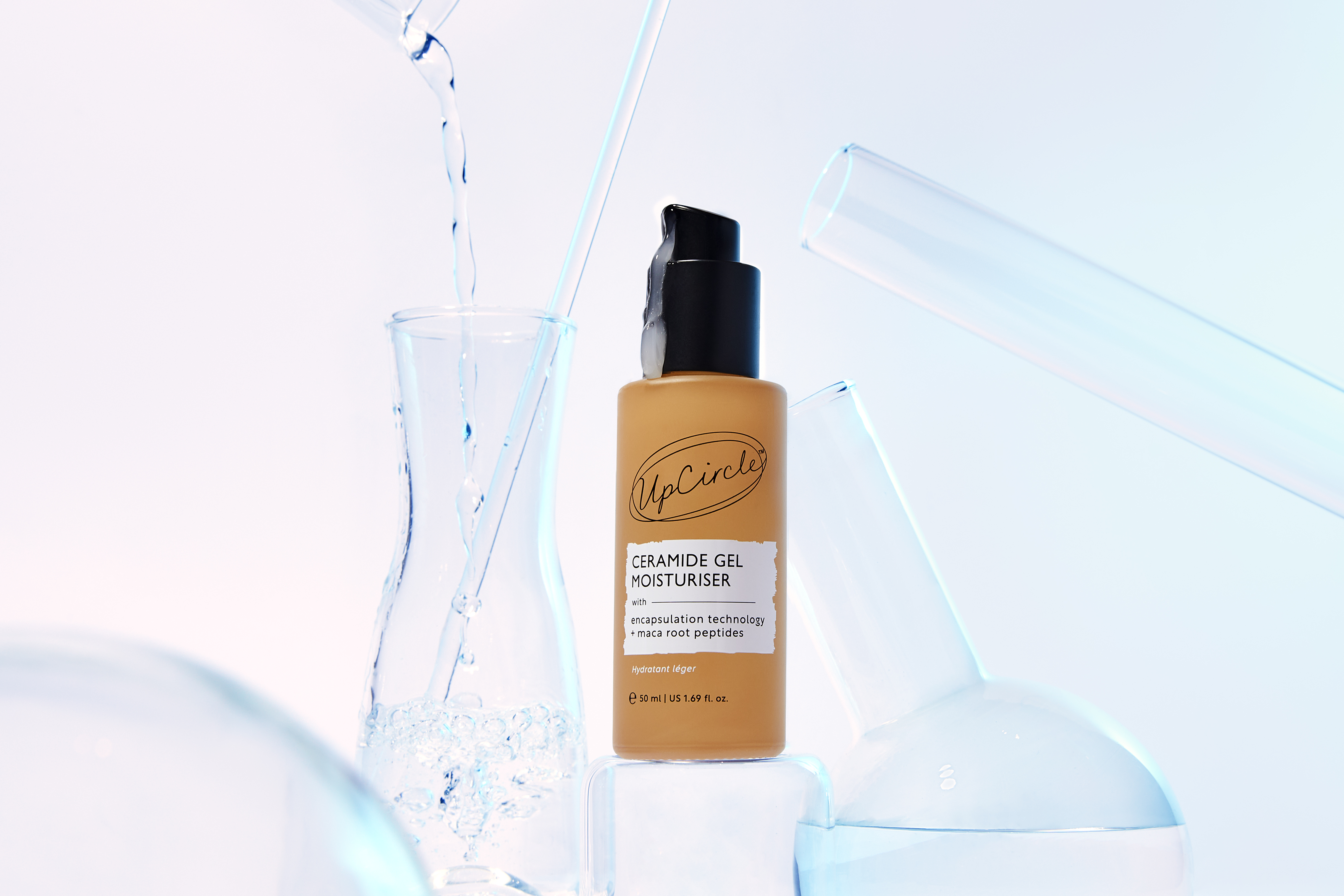 A bottle of UpCircle Ceramide Gel Moisturiser sits among laboratory beakers with water pouring into one.