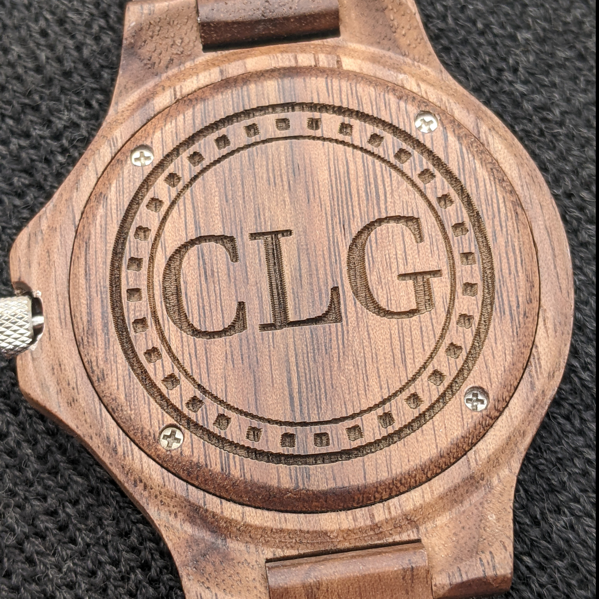 Wooden watch back with 'CLG' engraving and metal screws.