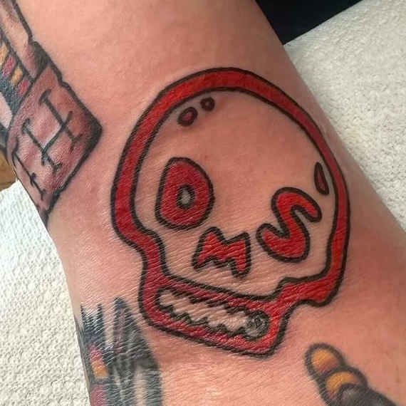 A close-up of a red outlined skull tattoo with letters D, M, and S for facial features.