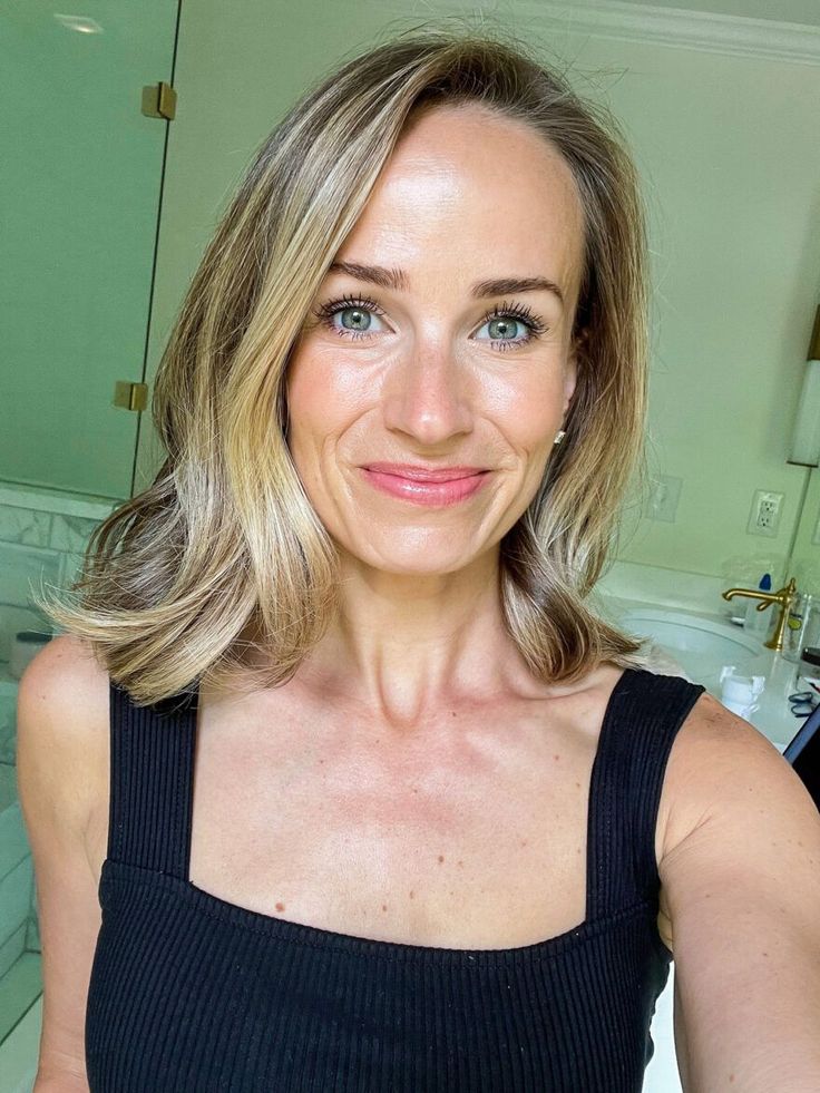 Person with shoulder-length blonde hair smiling in a bathroom.