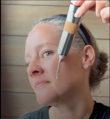 Person applying cream to face from a tube.