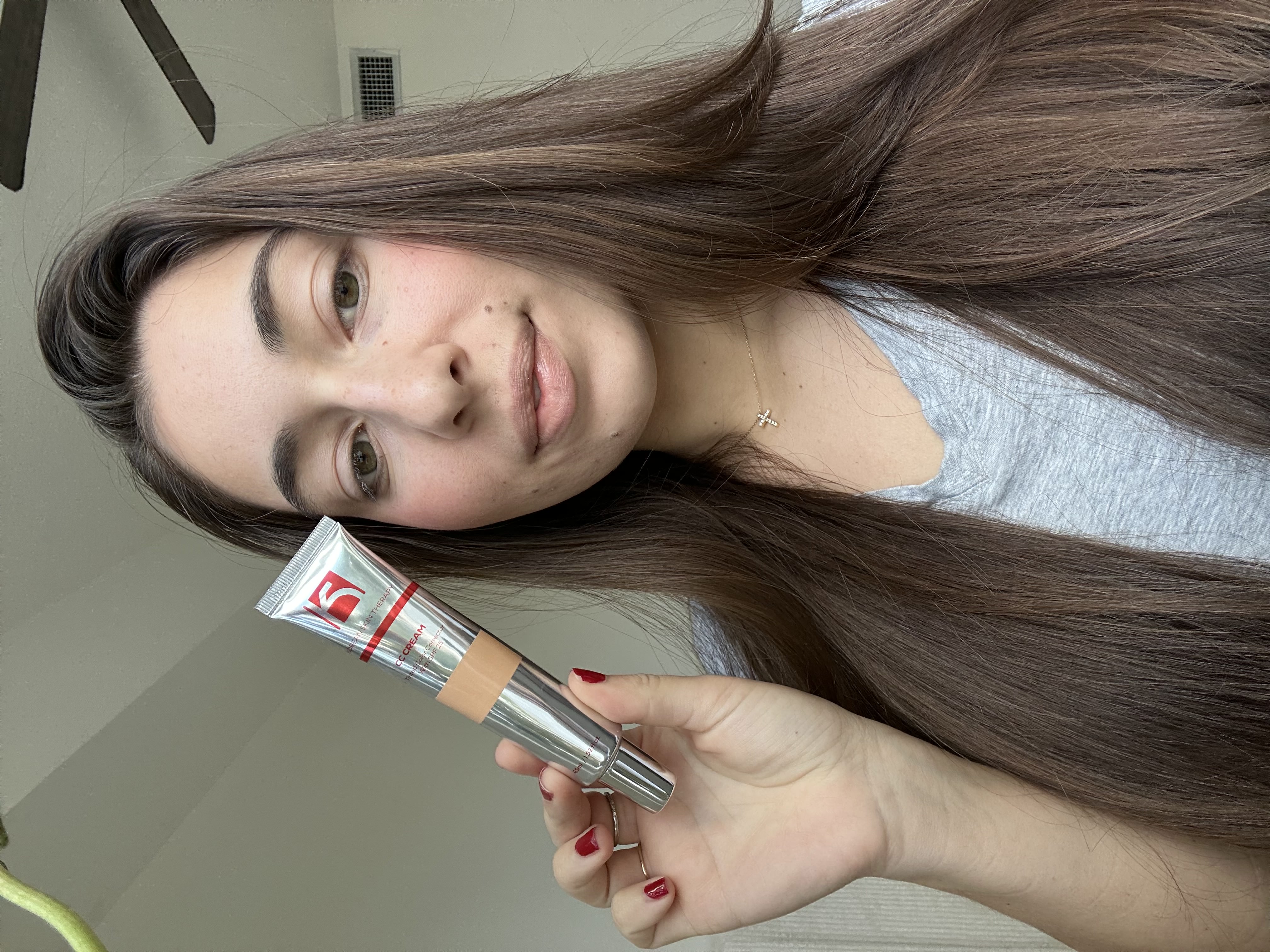 Person holding a tube of cream, with long hair and a gray shirt.