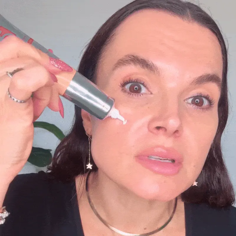 Person applying cream under their eyes from a tube.
