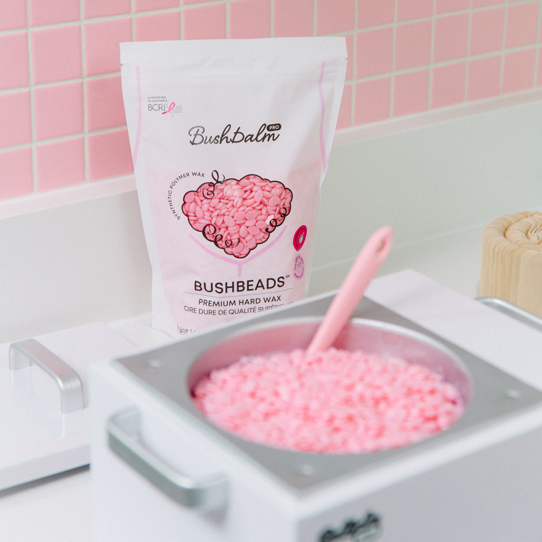A bag of BushBalm pink wax beads sits behind a wax warmer filled with the same beads.