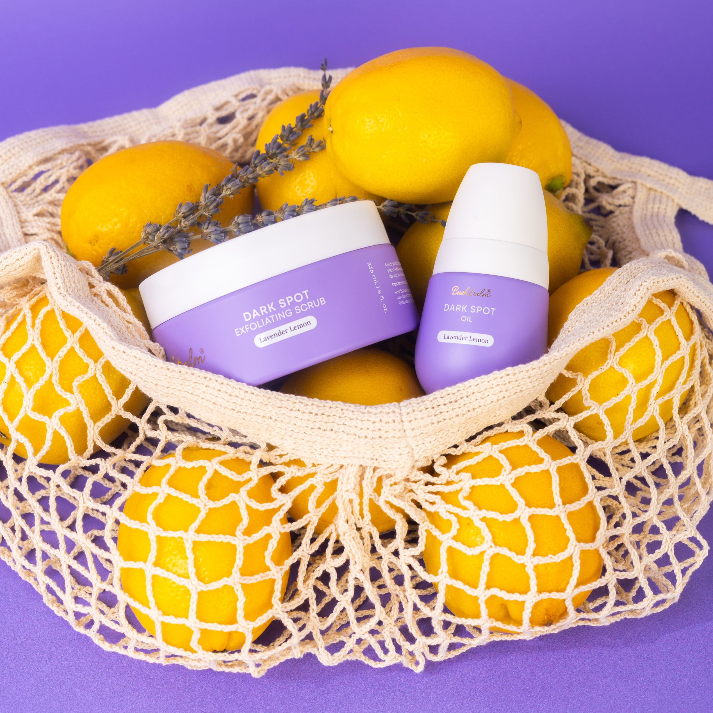 Net bag with lemons, lavender, and skincare products on a purple background.