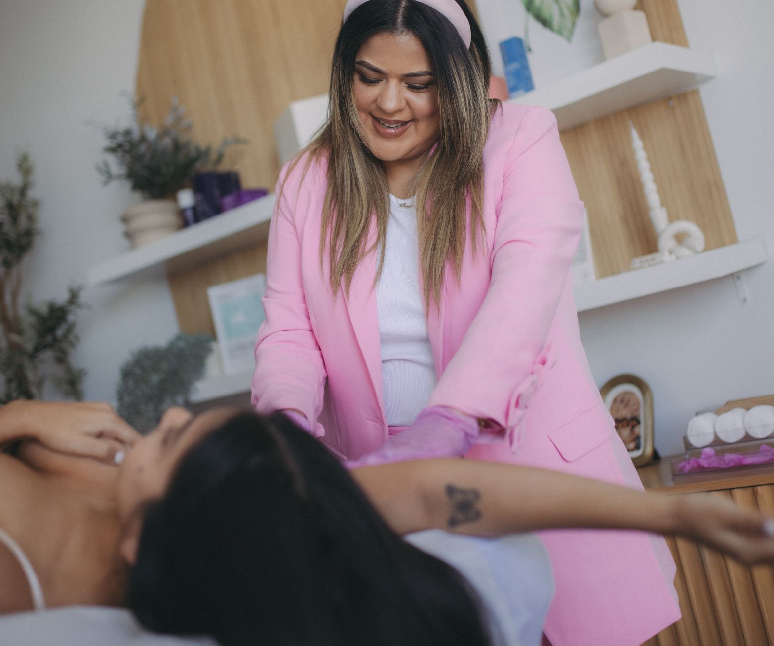 Woman in pink suit assisting another woman lying down in a room.