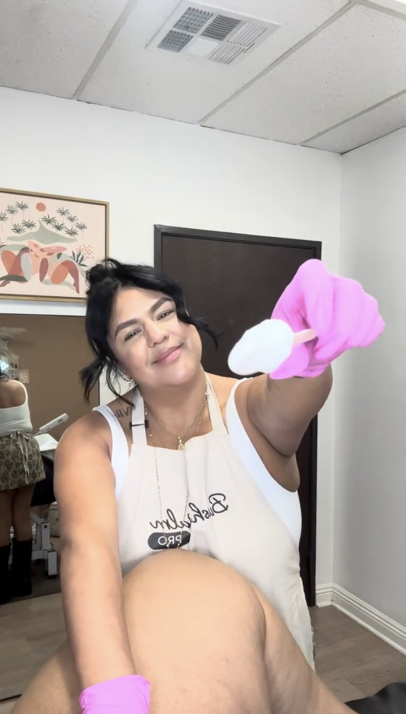 Person in apron holding a cotton pad, smiling in a room.