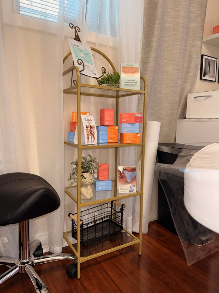 A gold shelving unit displays beauty products next to a black rolling stool in a treatment room.