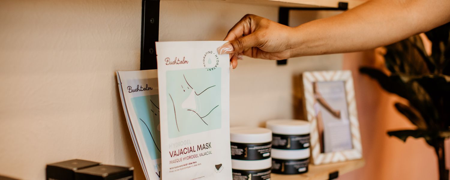 Person holding a skincare product beside a vajacial mask kit near a window.