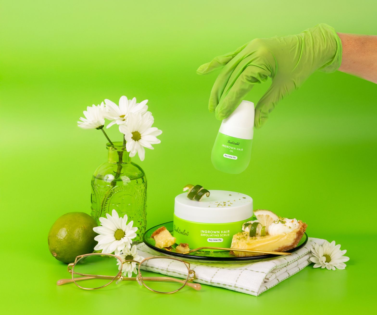 Green-themed setup with skincare products, daisies, lime, pie, and glasses on a green background.