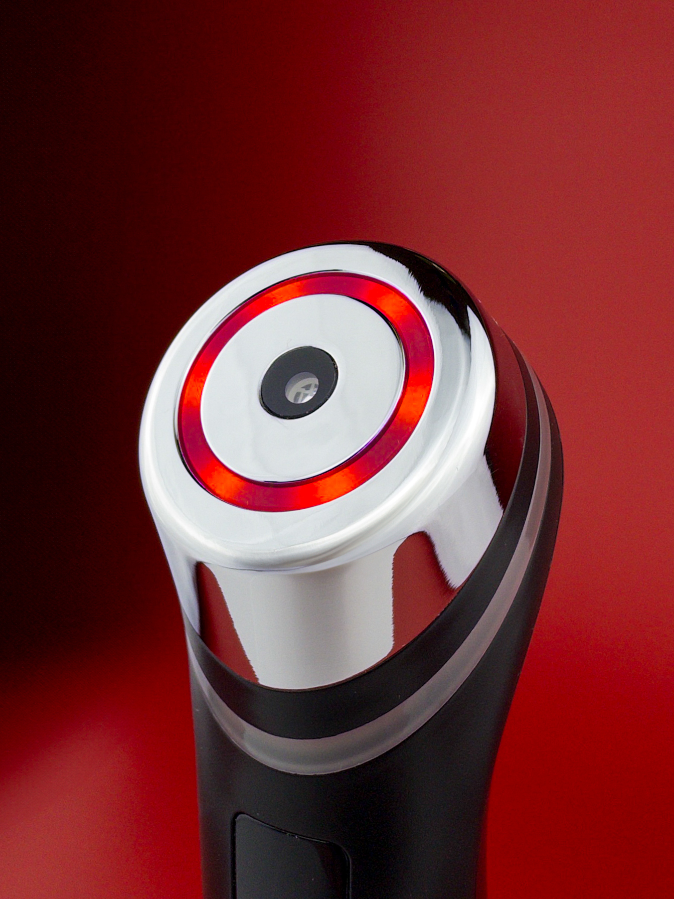 Close-up of a metallic device with a red circular light on a red background.