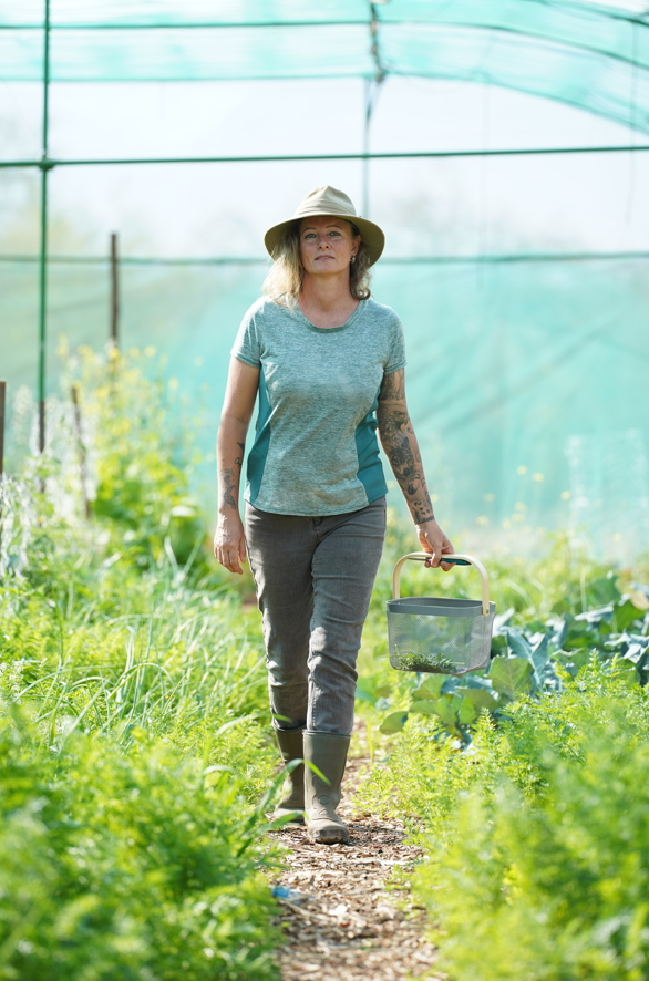 Person walking in a greenhouse garden holding a basket.