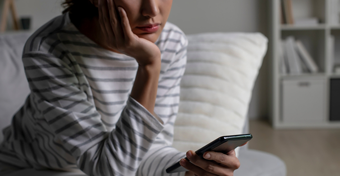 A person in a striped shirt sits on a couch looking at their phone, resting their chin on their hand.