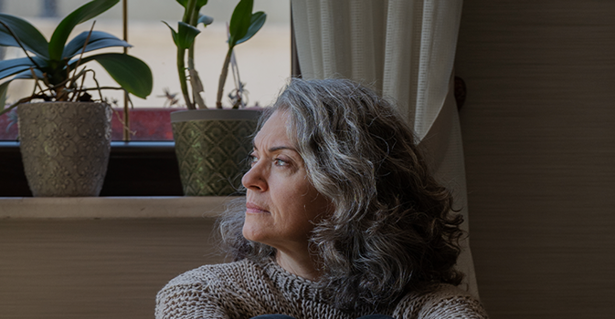 A woman with gray curly hair and a knit sweater looks thoughtfully off to the side.