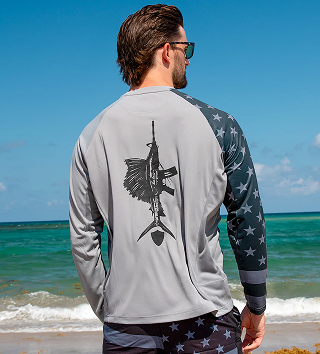 Man wearing a long-sleeve shirt with a fish design, standing by the ocean.