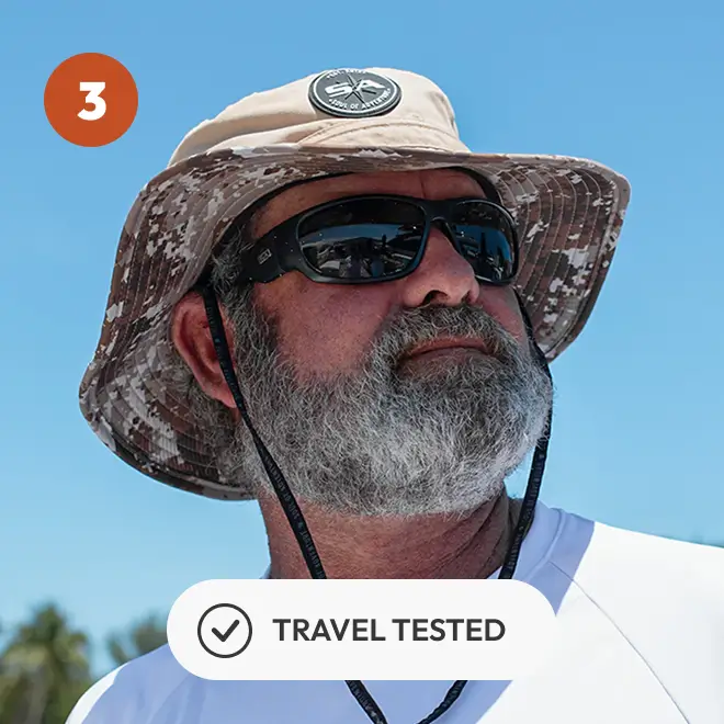 Man with sunglasses and camo hat under blue sky, labeled 'Travel Tested.'