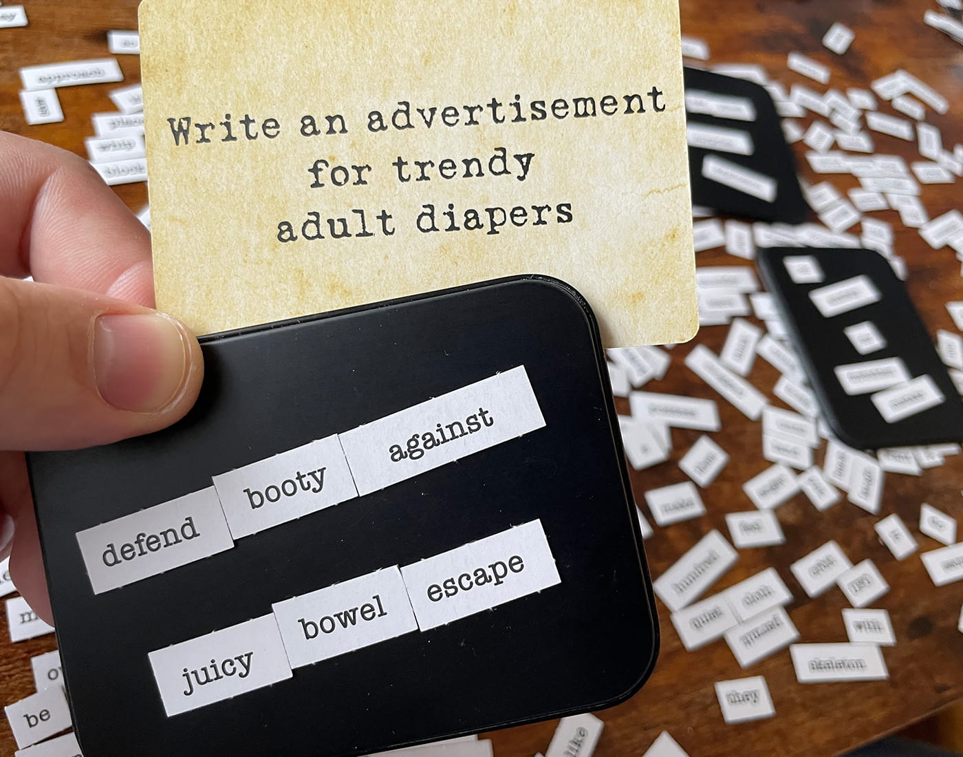 A person playing a word game with a prompt card reading 'Write an advertisement for trendy adult diapers'.