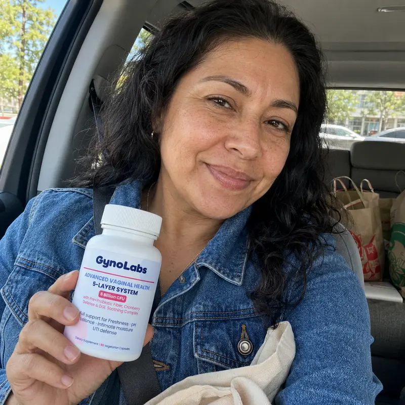 A smiling woman in a car holds up a white bottle of GynoLabs Advanced Vaginal Health supplements.