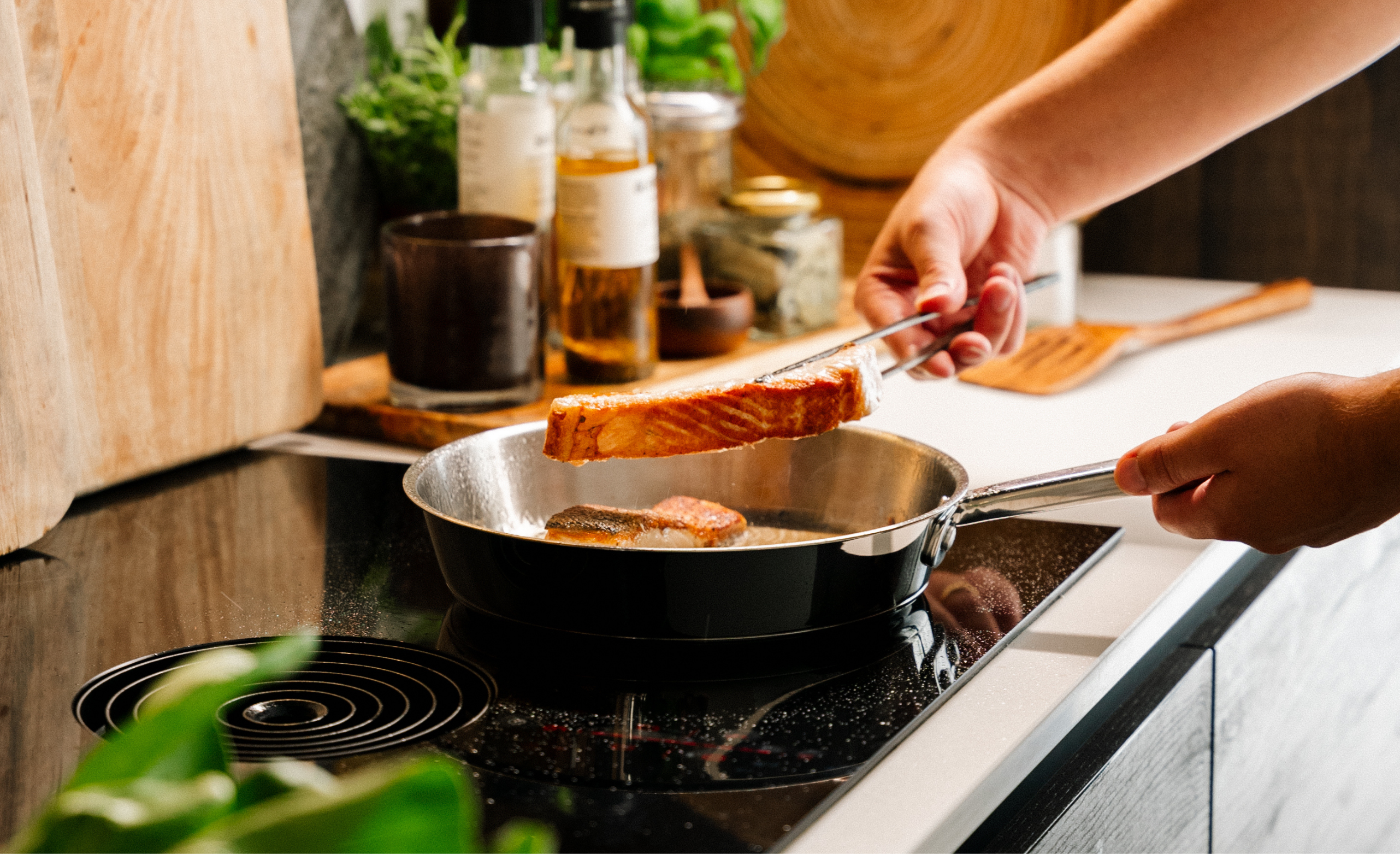 Person cooking salmon in a pan on a stovetop.