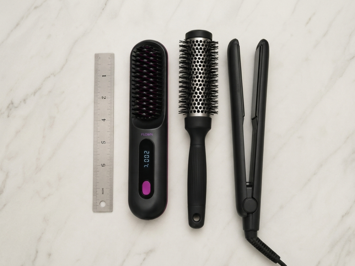 A ruler, a straightening brush, a round brush, and a flat iron on a marble surface.