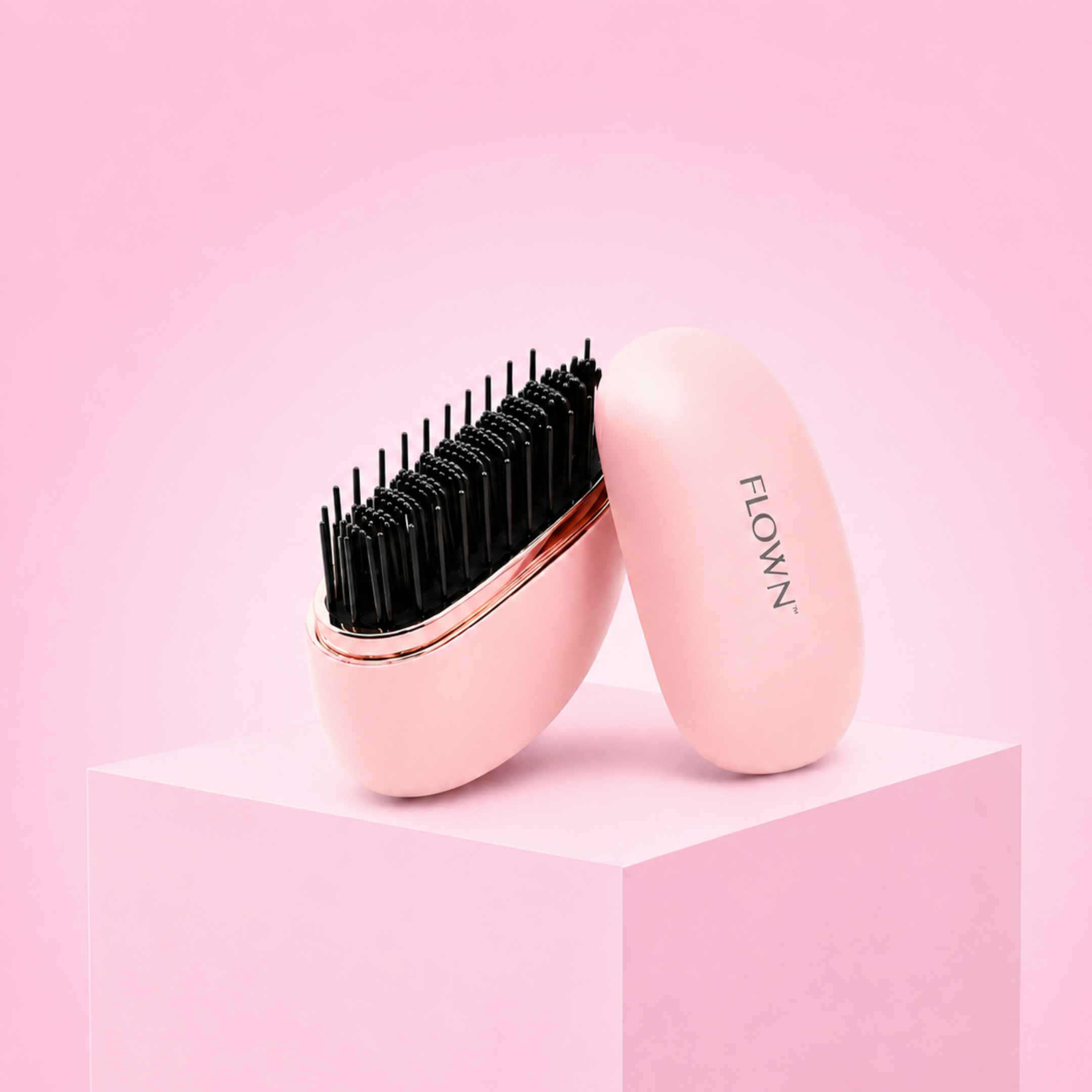 A pink and rose gold detangling hairbrush with its cover, resting on a pink block against a pink background.