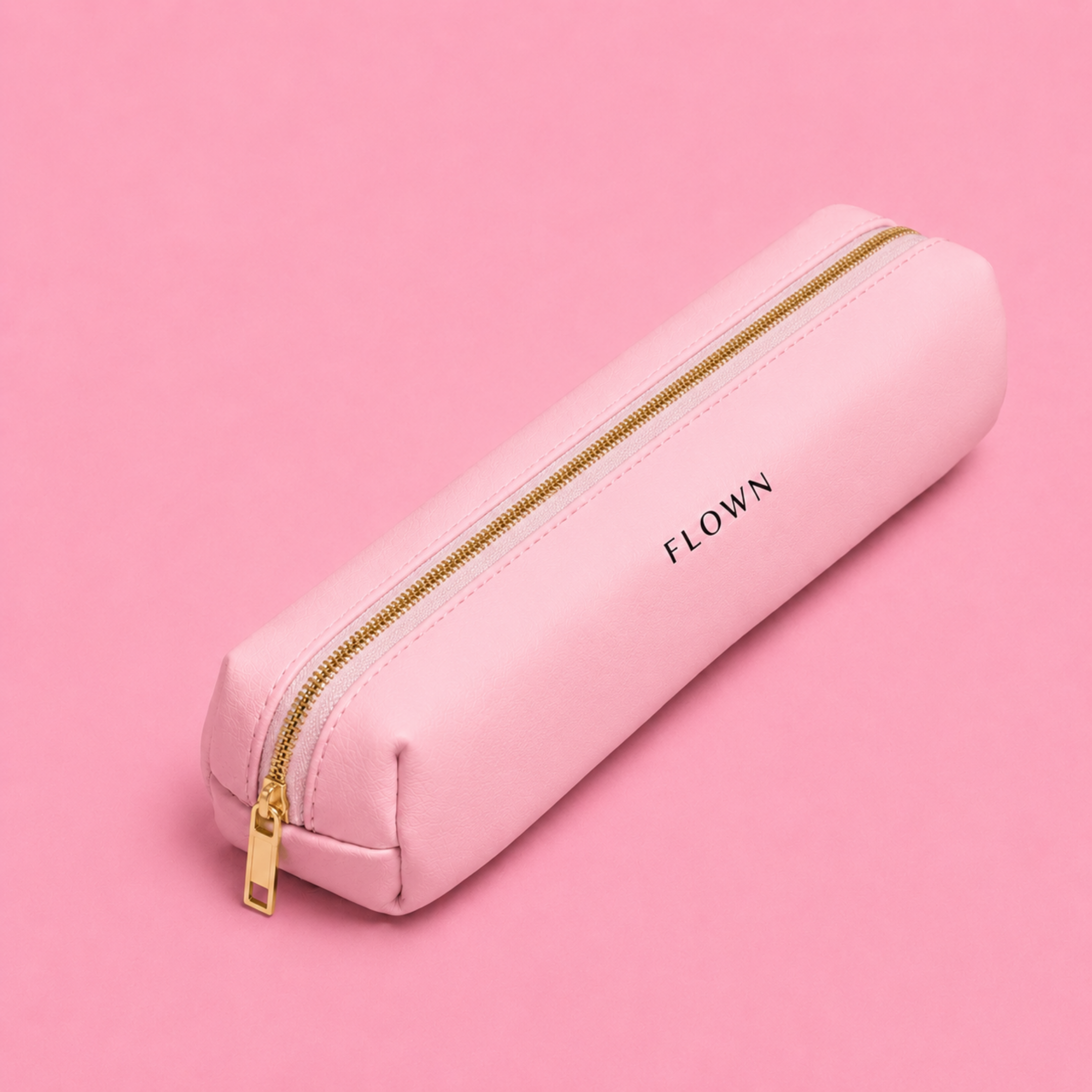 A pink pencil case with a gold zipper and the word FLOWN, on a pink background.