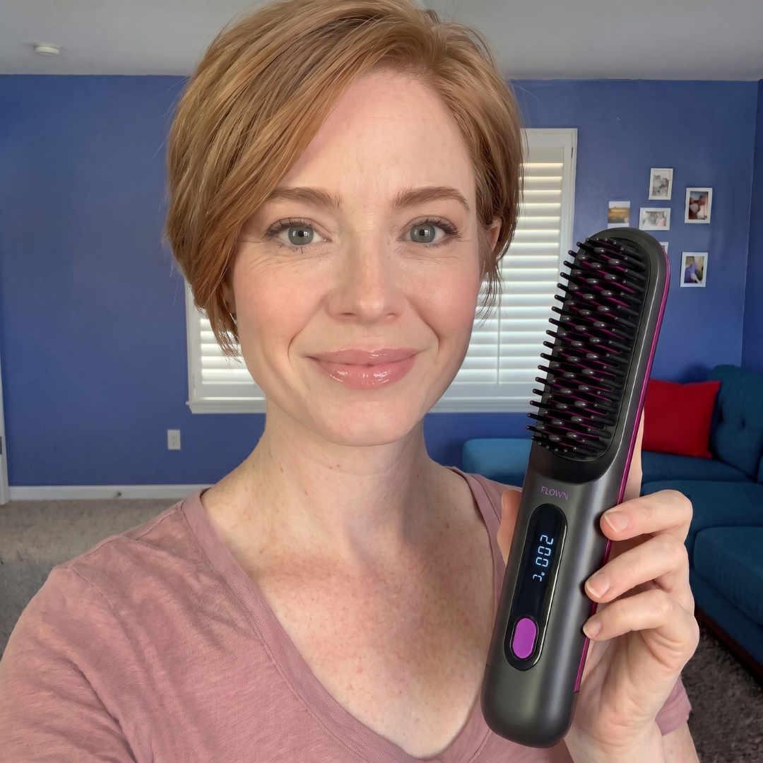 A smiling woman with short red hair holds up a black heated straightening brush.