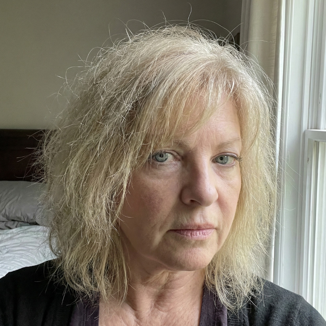A headshot of a woman with messy blonde hair and light-colored eyes looking at the camera.