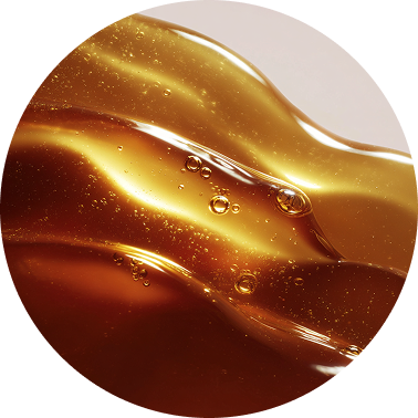 A circular close-up of a thick, golden, viscous liquid with small bubbles.