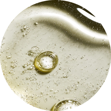 A circular, macro photograph of a transparent, yellowish liquid with several bubbles.