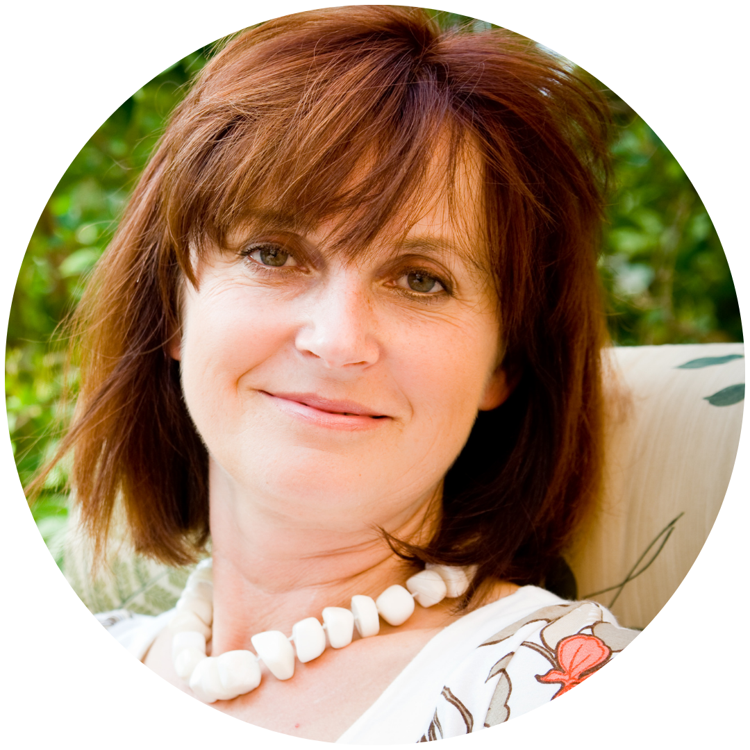 A person with brown hair and a white necklace, smiling outdoors.