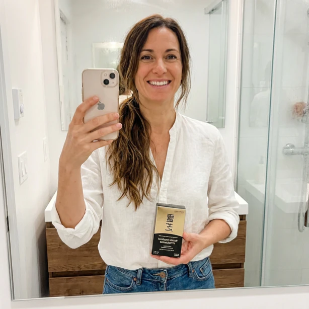 Person in white shirt taking a mirror selfie holding a product box.