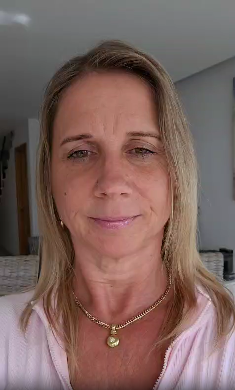 A woman with blonde hair wearing a pink top and gold necklace.