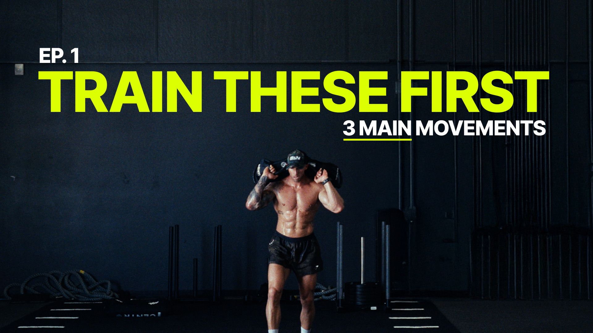 A muscular man holds a weighted bag on his shoulders, with text overlay reading 'Train These First'.