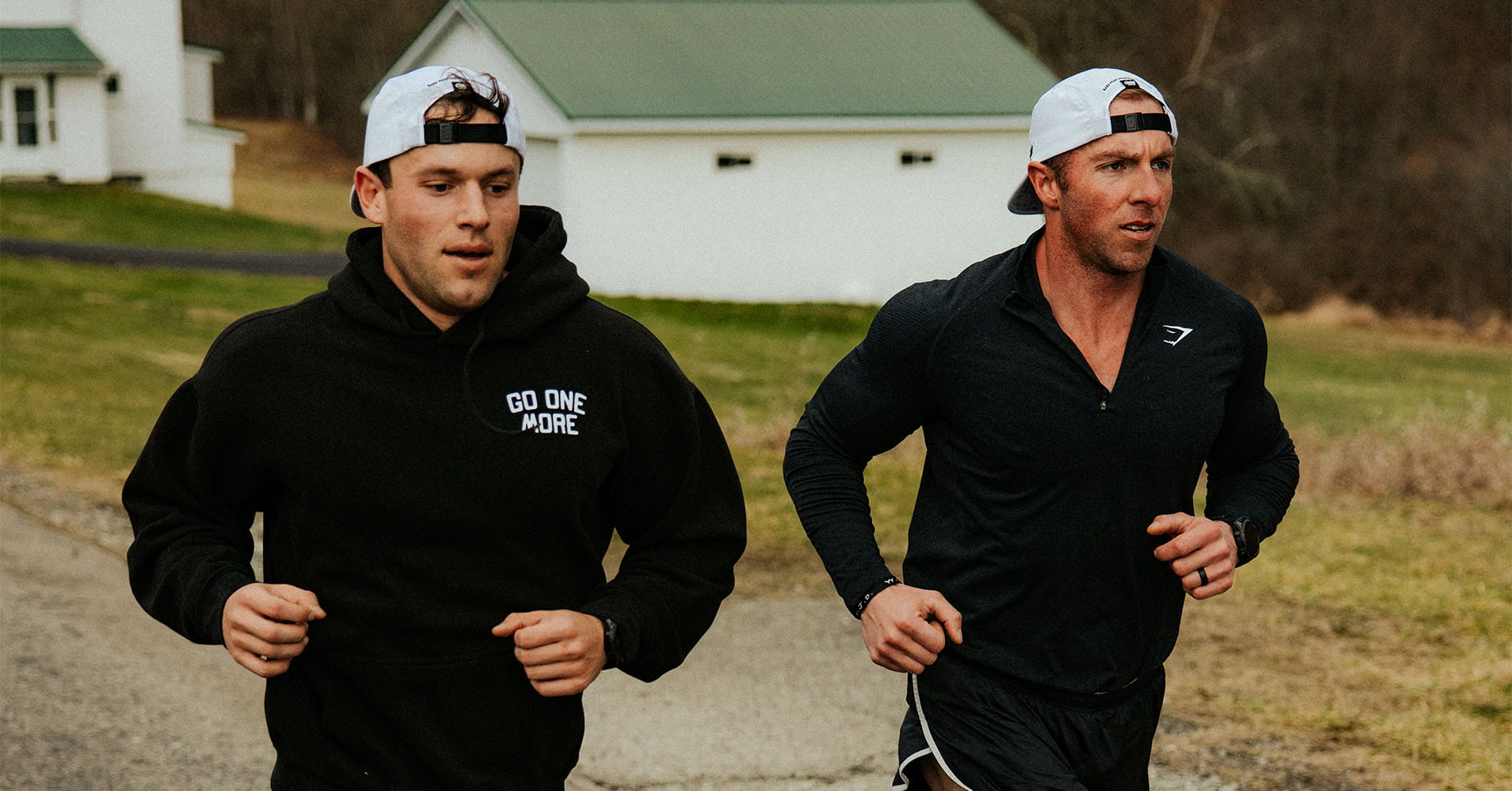 Two men in athletic wear and baseball caps are running side-by-side outdoors.