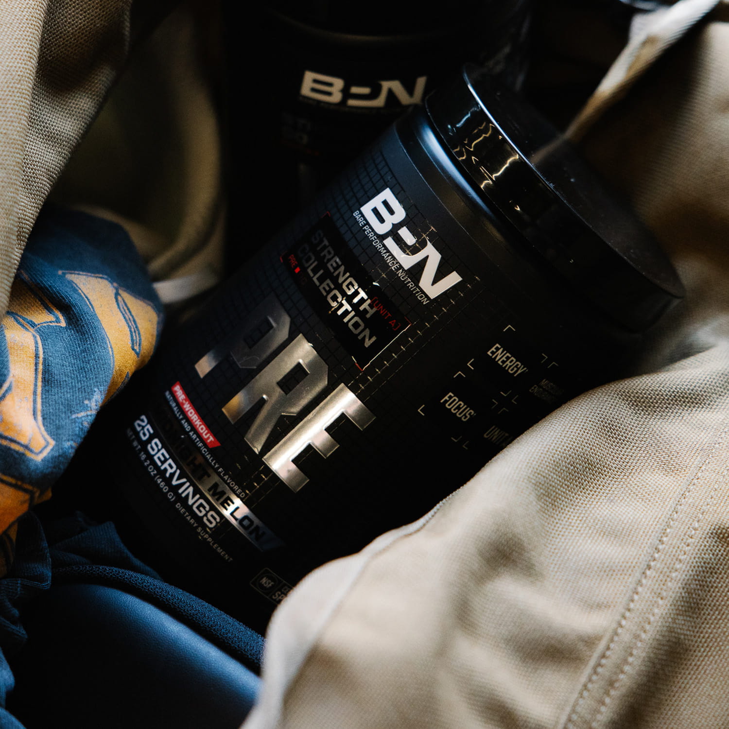 A black tub of BPN Pre-Workout supplement in Flight Melon flavor sitting inside a tan canvas bag.