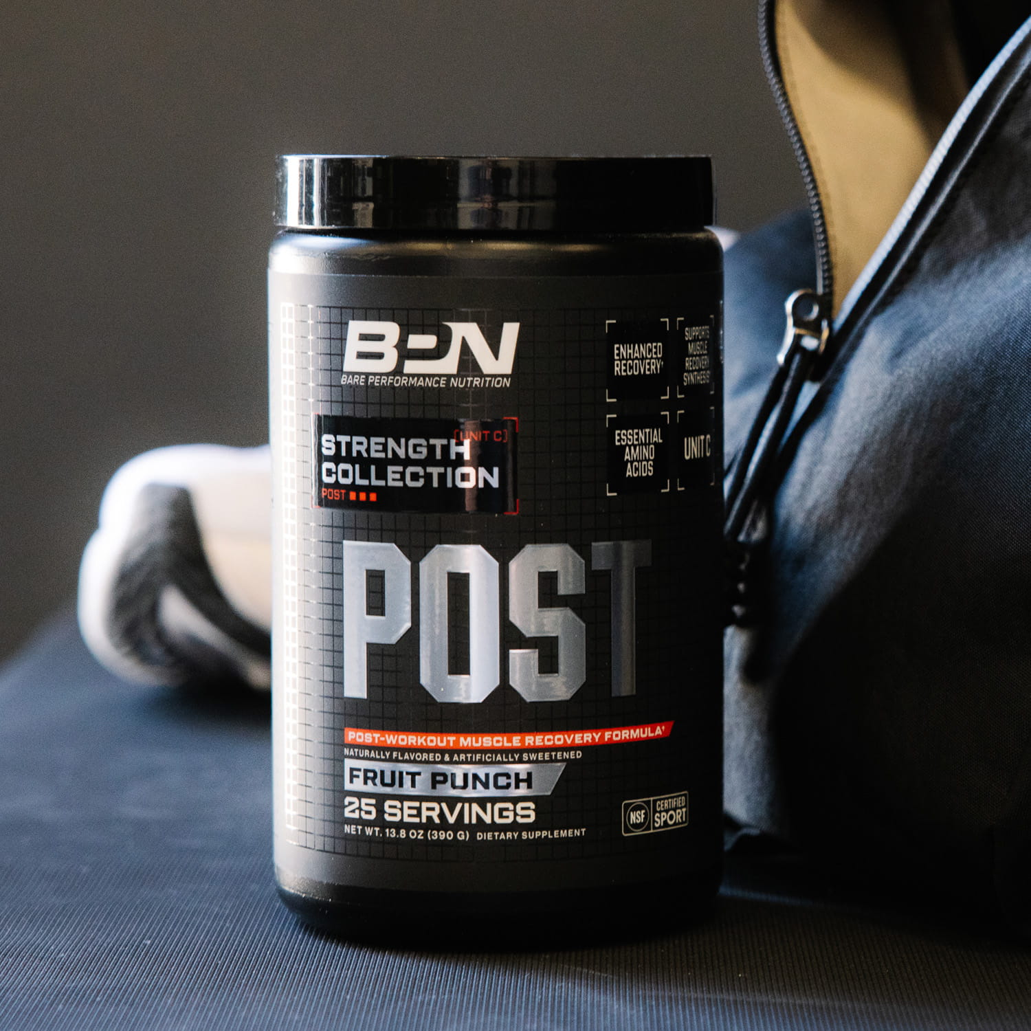 A black tub of BPN Post-Workout Fruit Punch supplement sits on a mat next to a gym bag.